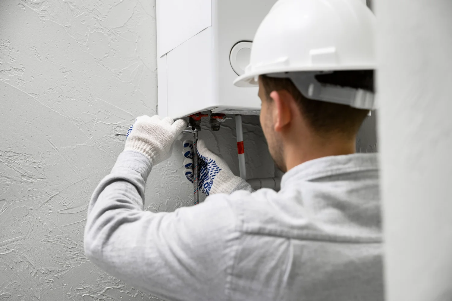 Plumber repairing wall-mounted boiler unit indoors
