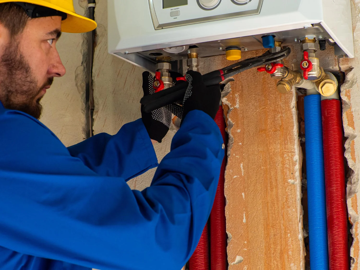 Plumber repairing domestic boiler and pipework indoors