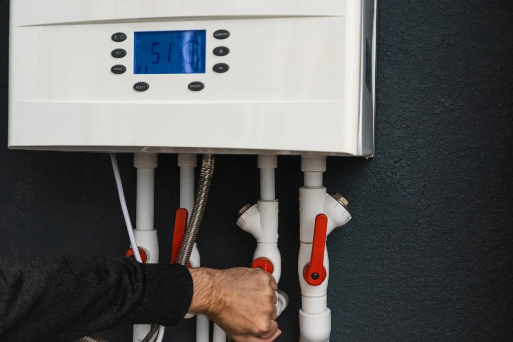 Person adjusting valves beneath a wall-mounted boiler