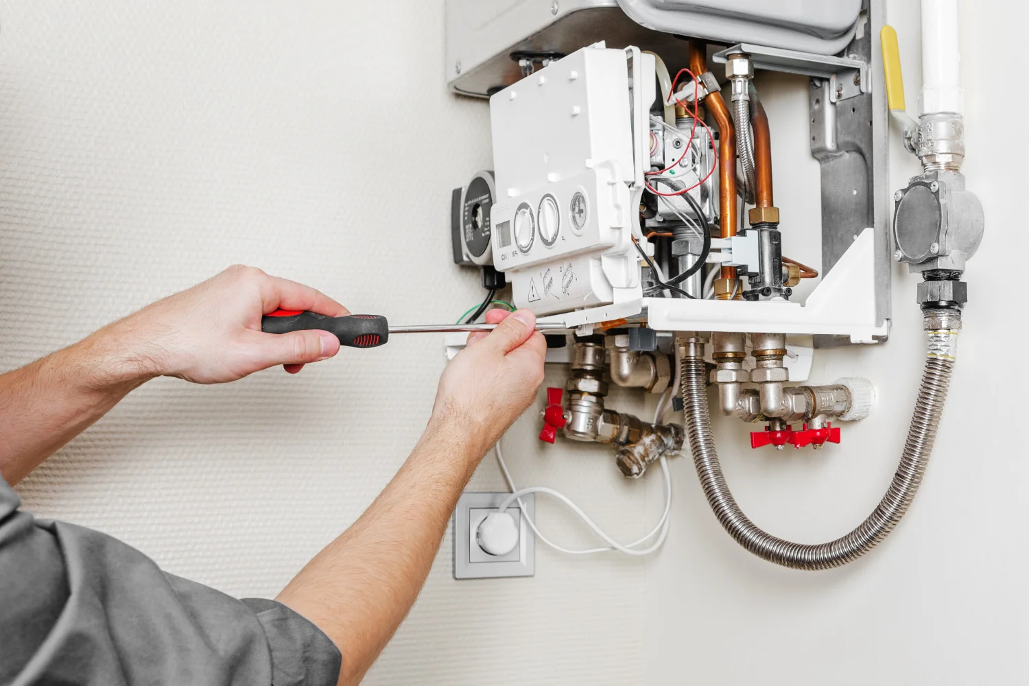 Technician repairing wall-mounted gas boiler with screwdriver