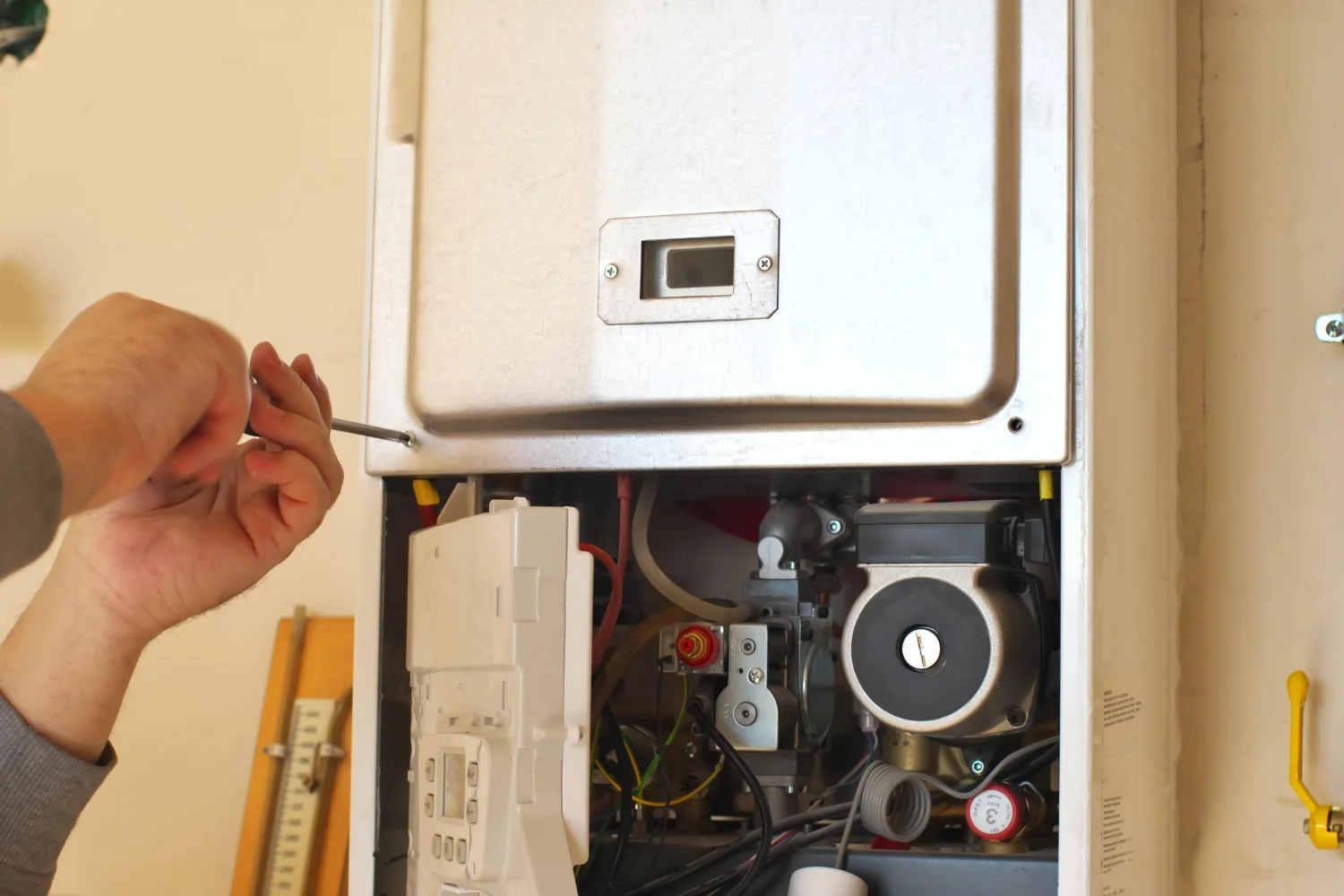 Technician opening domestic boiler panel with screwdriver